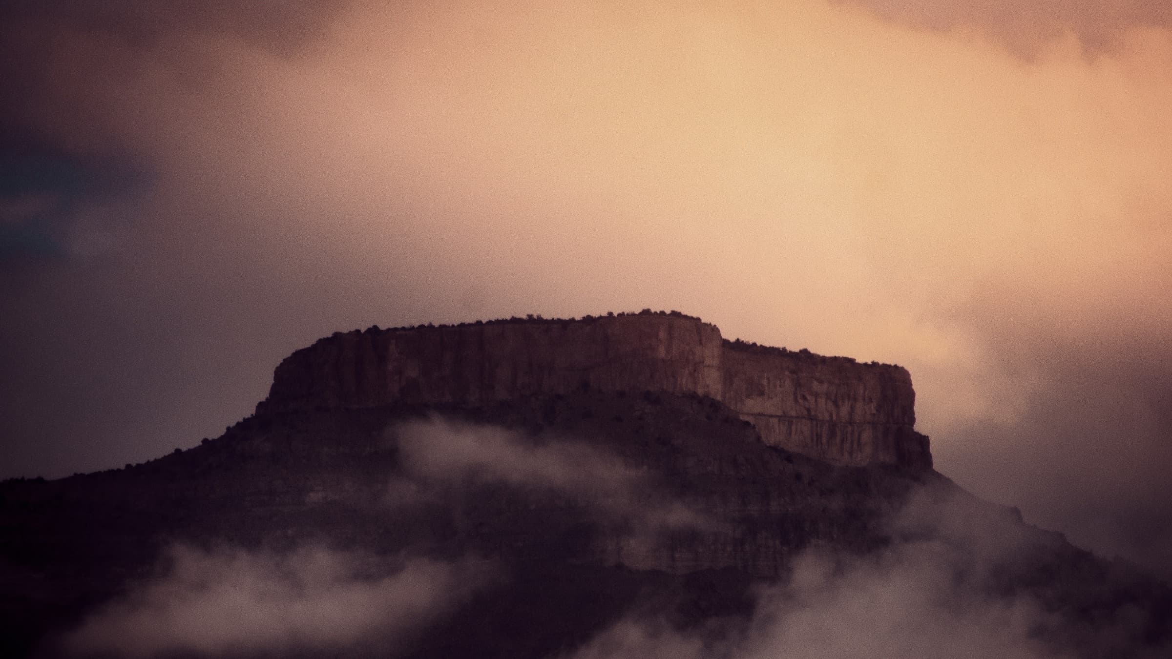 A massive flat-topped mountain emerging through storm clouds